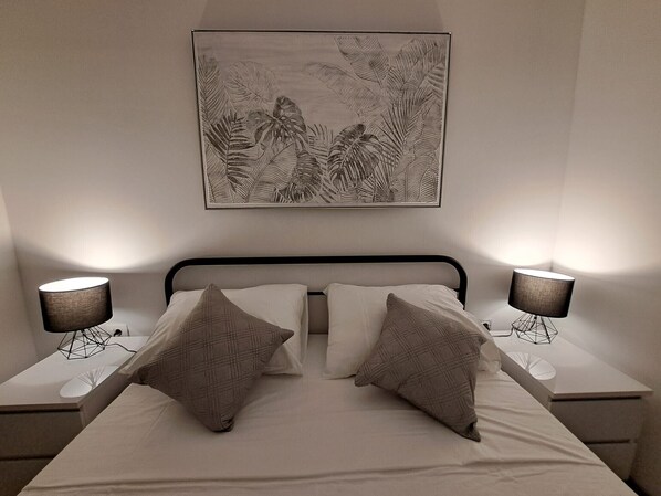 Un dormitorio con una cama, dos mesitas de noche, dos lámparas y una obra de arte colgada en la pared.