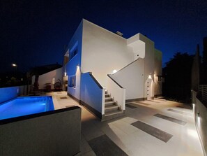 A modern house with a swimming pool, a staircase, and a well-lit exterior at night.
