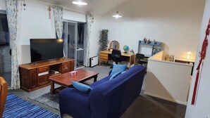 Een woonkamer met een televisie, bank, salontafel en een bureau met een computer.