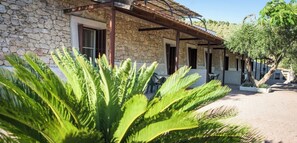 Un bâtiment en pierre doté d’un patio couvert, d’un espace extérieur aménagé pour s’asseoir et d’un arbre au premier plan.