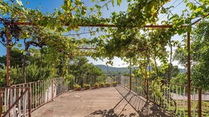 Un espacio al aire libre techado con barandilla de metal, plantas en macetas y vistas del paisaje circundante.