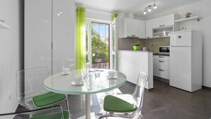 Una cocina moderna con armarios blancos, una mesa de comedor de vidrio con sillas verdes y vistas al exterior.