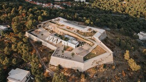 Vista aérea de un complejo fortificado con varios edificios, senderos y zona boscosa circundante.
