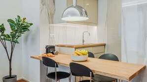 A compact kitchen with a wooden countertop, two black chairs, a bowl of fruit, a coffee maker, and a hanging light fixture.