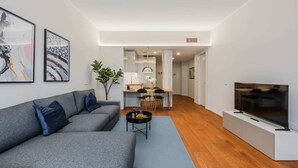 A modern living room with a grey sofa, a coffee table, a flat-screen TV, and artwork on the walls.