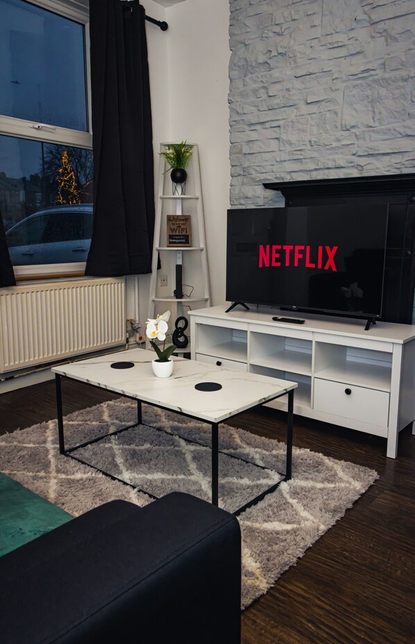A living room with a TV, white furniture, a potted plant, and a Christmas tree.