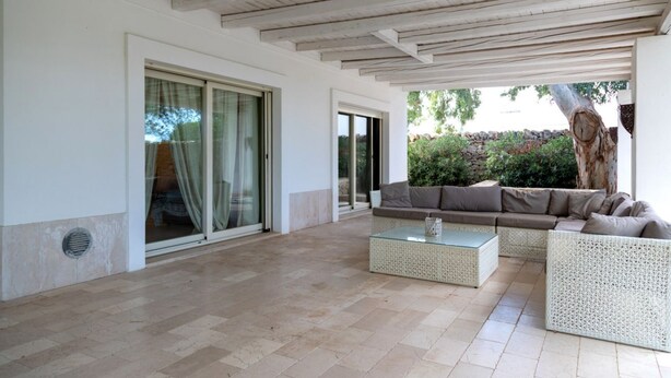 A covered outdoor area with a sofa and a coffee table, a sliding glass door, and a tree trunk. - Villa Luna 20 meters from the sea in Punta Prosciutto (Punta Prosciutto)