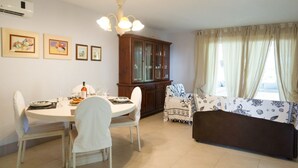 A dining area with a round table, white chairs, a wooden cabinet, and a sofa with a patterned cover. - Villa Luna 20 meters from the sea in Punta Prosciutto (Punta Prosciutto)