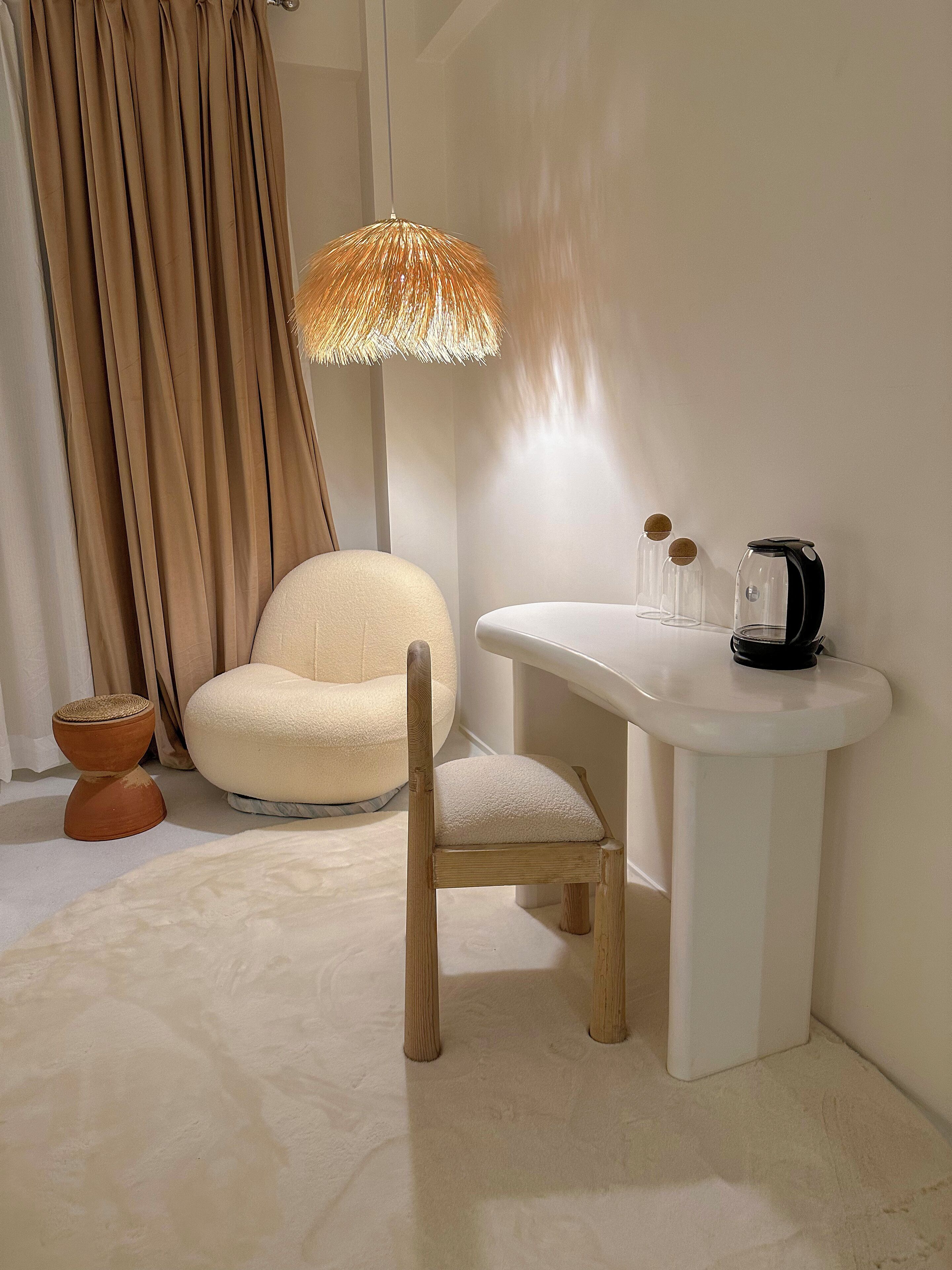 Ein modernes Zimmer mit einem runden Sessel, einem weißen Beistelltisch, einer Stehlampe und einer Kaffeemaschine.