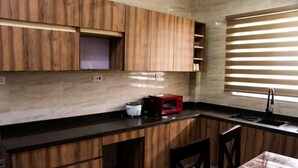 Una cocina moderna con armarios de madera, encimera negra, microondas rojo y una ventana con persianas.
