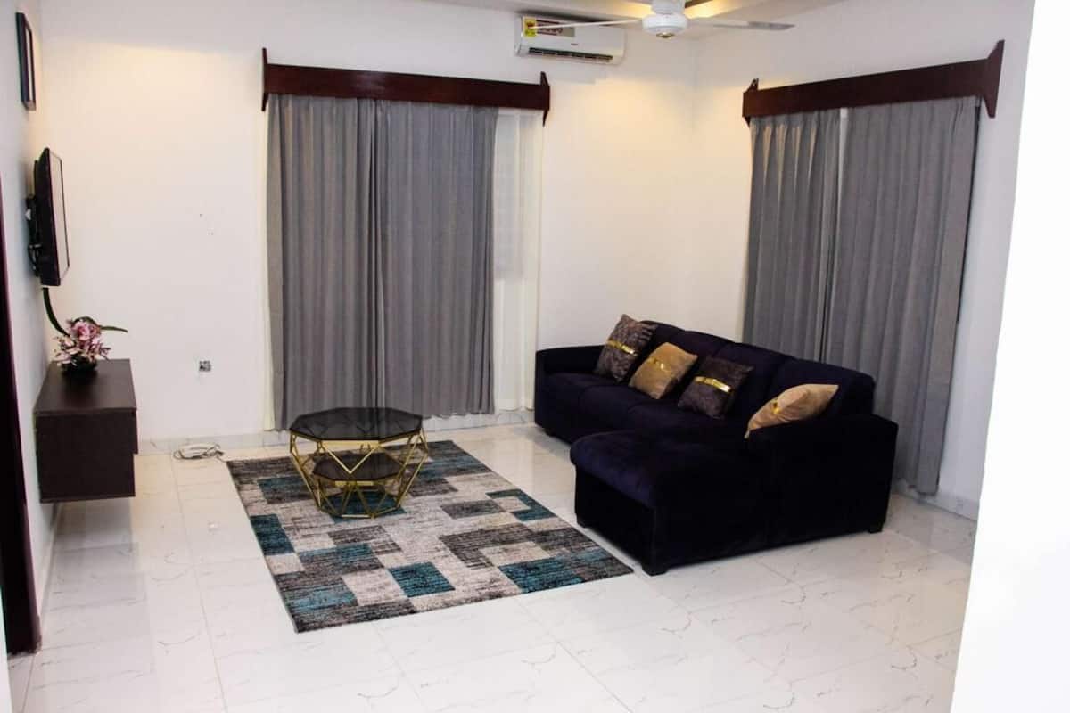 Una sala de estar con un sofá de color oscuro, una mesita redonda y un tapete a cuadros.