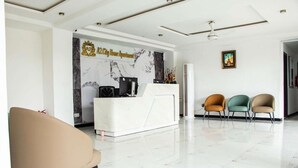 Un área de recepción moderna con una pared de mármol y un mostrador de recepción. Hay tres sillas en primer plano y un cuadro en la pared.