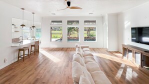 A spacious living room with a large sectional sofa, a kitchen area with a bar, and a TV on the right. - Charming & Bright Retreat - Luxe Pool - Golf Views! (Humble)
