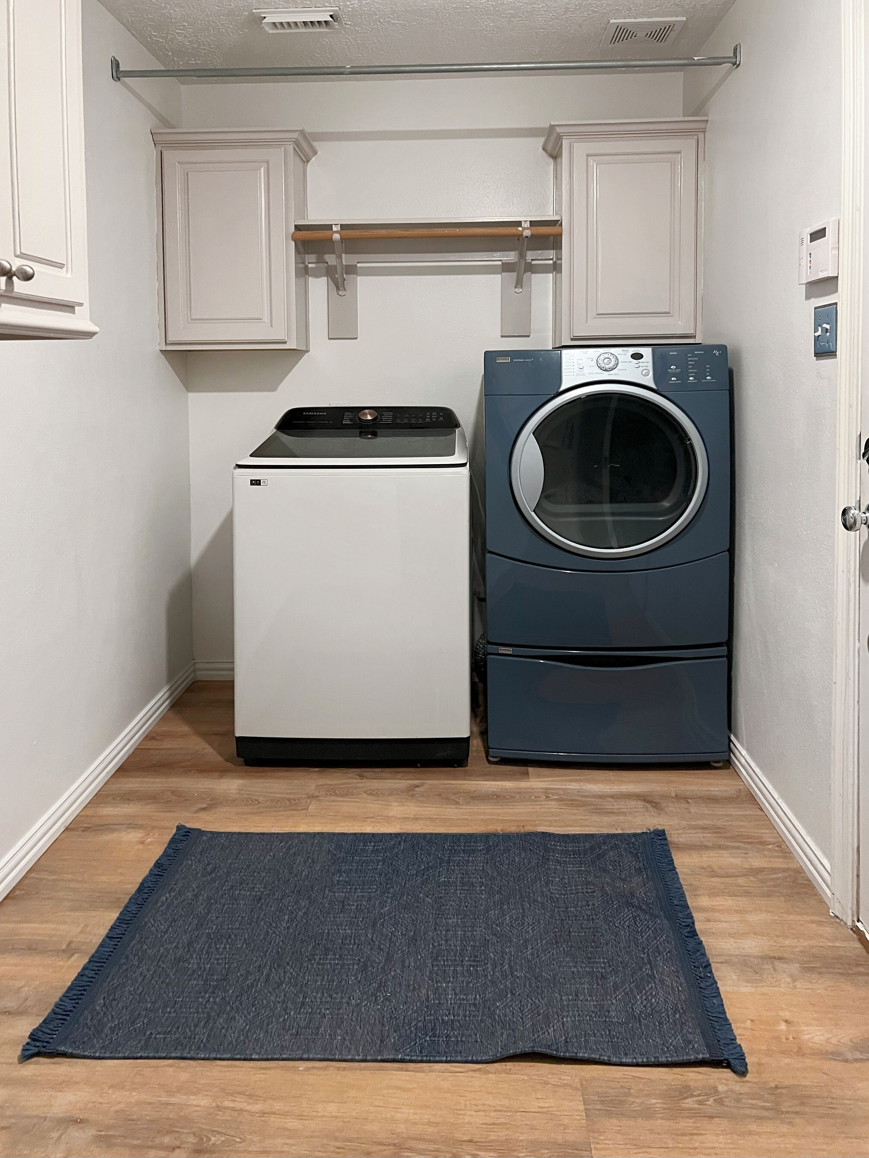 Une buanderie équipée d’un lave-linge et d’un sèche-linge, avec un petit tapis et des meubles de rangement blancs.