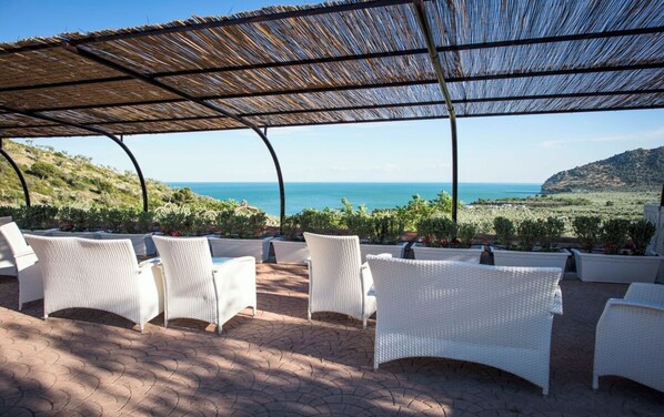 A covered outdoor seating area with white wicker furniture and a view of the sea.