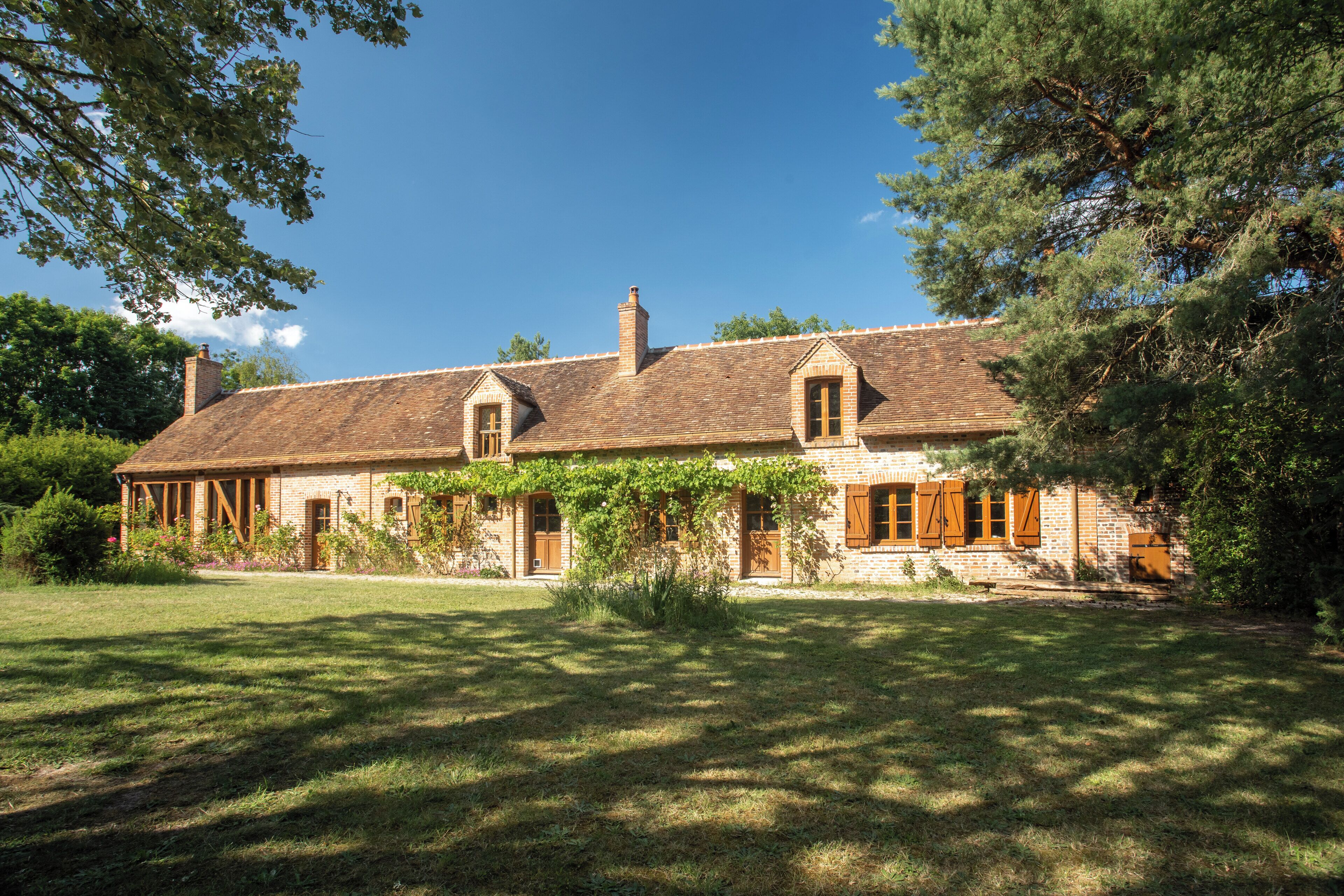 A two-story stone house with a sloped roof, wooden shutters, and a well-maintained lawn.
