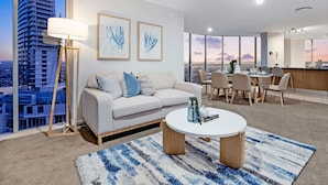 Una sala de estar moderna con sofá, mesa de centro y comedor. Amplias ventanas ofrecen vistas a la ciudad.