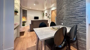 Ein moderner Essbereich mit Steinwand, einer Couch und einem Fernseher im Hintergrund.