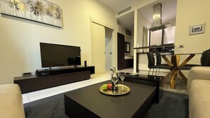 A modern living room with a flat-screen TV, a dark coffee table with a decorative plate, and a seating area with a sofa and chairs. - TQ Plaza 314 Suite (Budva)