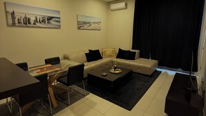 A modern living room with a sofa, coffee table, and dining area. There are two paintings on the wall and an air conditioning unit. - TQ Plaza 314 Suite (Budva)