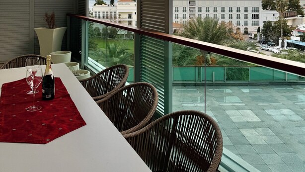 A balcony with a table set for two, overlooking a cityscape with mountains and buildings. - TQ Plaza 314 Suite (Budva)