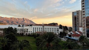 A hotel with a white facade, multiple balconies, and a view of mountains and a body of water. - TQ Plaza 314 Suite (Budva)