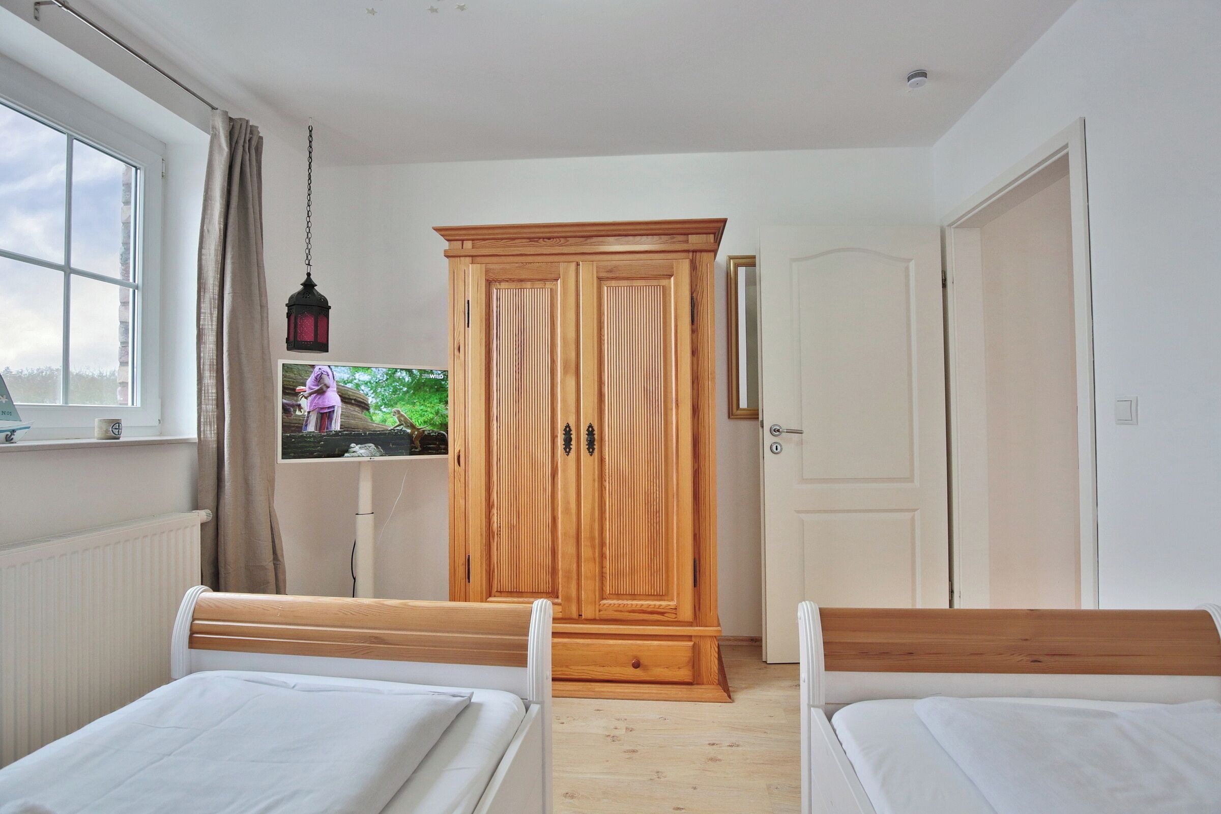 Un dormitorio con dos camas individuales, un armario de madera, un televisor y una ventana con cortinas.