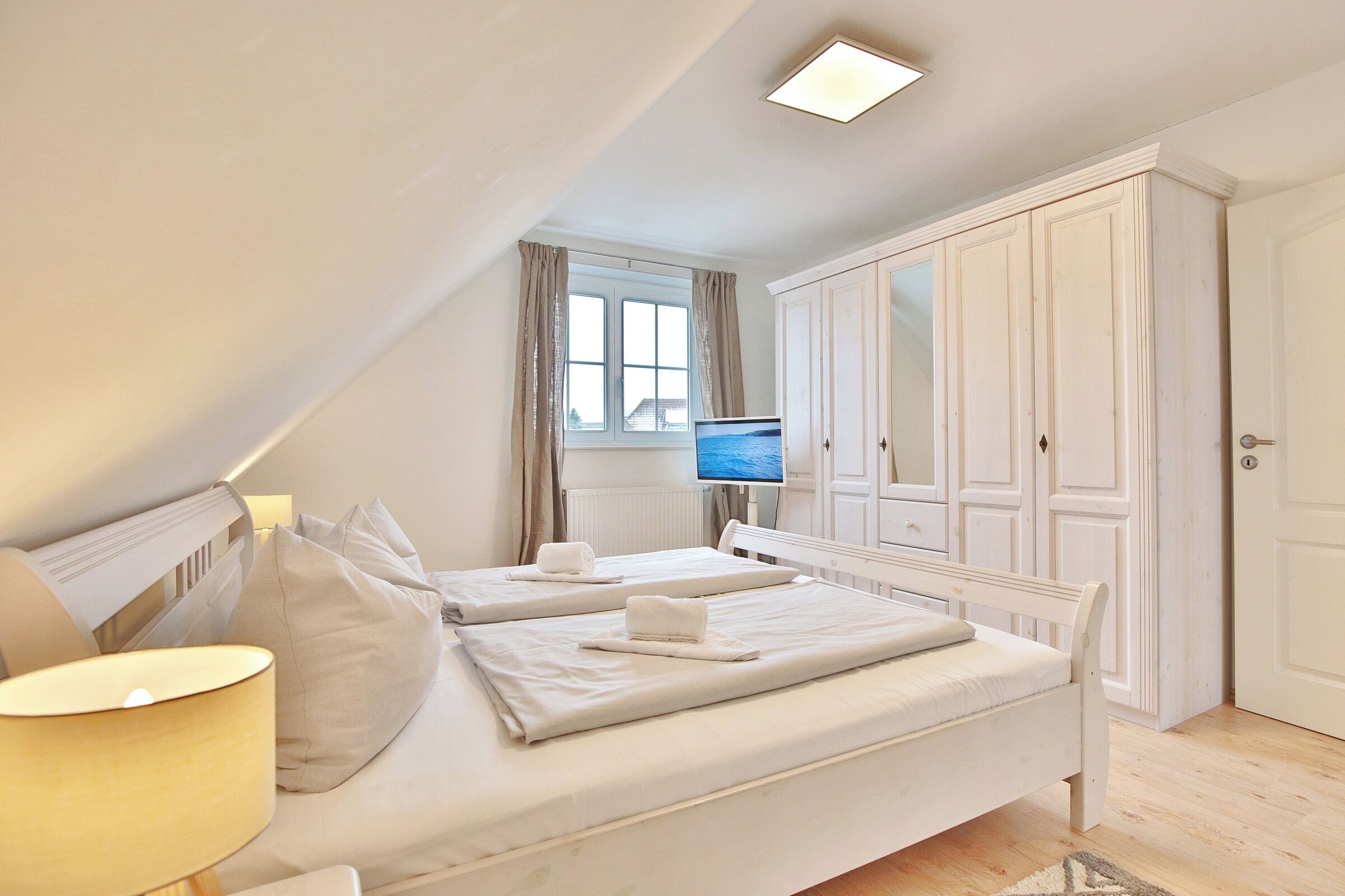 Une chambre avec deux lits, une grande armoire, une télévision et une fenêtre avec des rideaux.