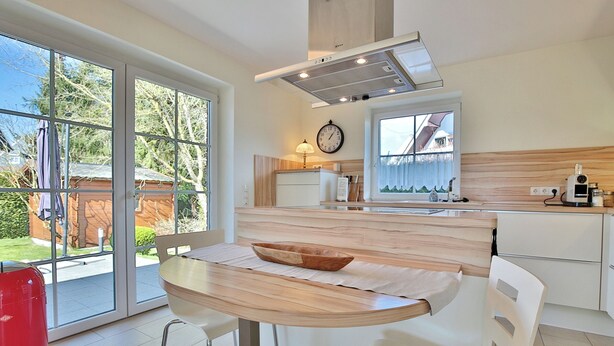 Eine moderne Küche mit Essbereich, großen Fenstern und Blick ins Freie.