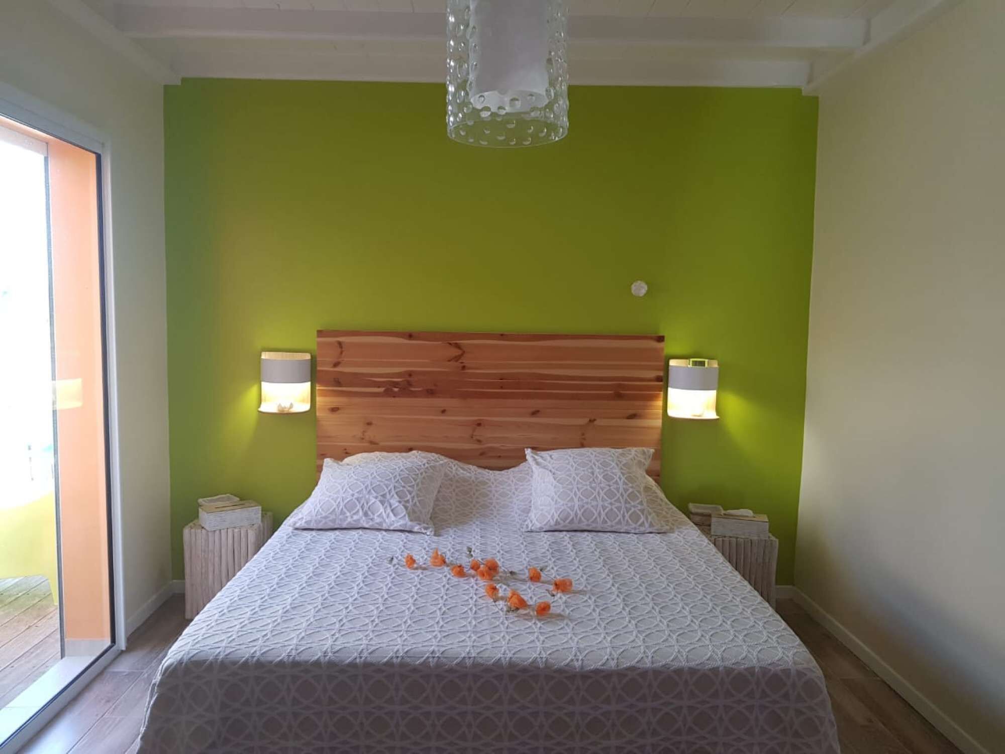 A bedroom with a wooden headboard, two bedside lamps, a bed with white bedding, and a green wall.