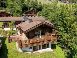 A wooden chalet with a balcony, surrounded by lush greenery.