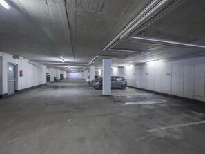 A multi-level parking garage with concrete floors and walls, overhead lighting, and several parked cars.