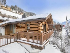 A wooden cabin with a balcony, surrounded by snow-covered landscape and mountains.