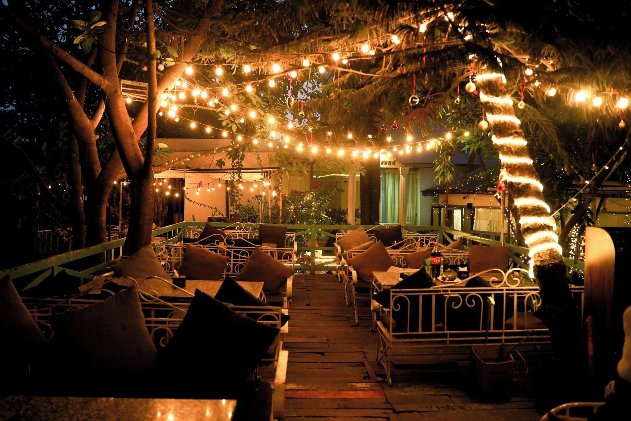 An outdoor seating area with tables and chairs, string lights, and a tree.