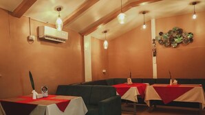 Een restaurant met tafels voorzien van rode tafelkleden, een wandairconditioner en hanglampen.