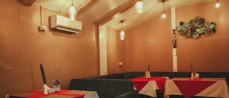 Un restaurante con mesas cubiertas de manteles rojos, una unidad de aire acondicionado montada en la pared e iluminación colgante.
