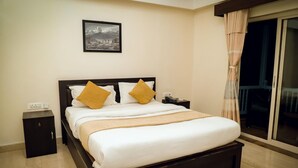 Een hotelkamer met een bed, nachtkastje, schilderij aan de muur en raam met gordijnen.