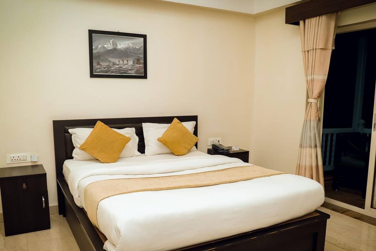 A hotel room with a bed, a nightstand, a painting on the wall, and a window with curtains.