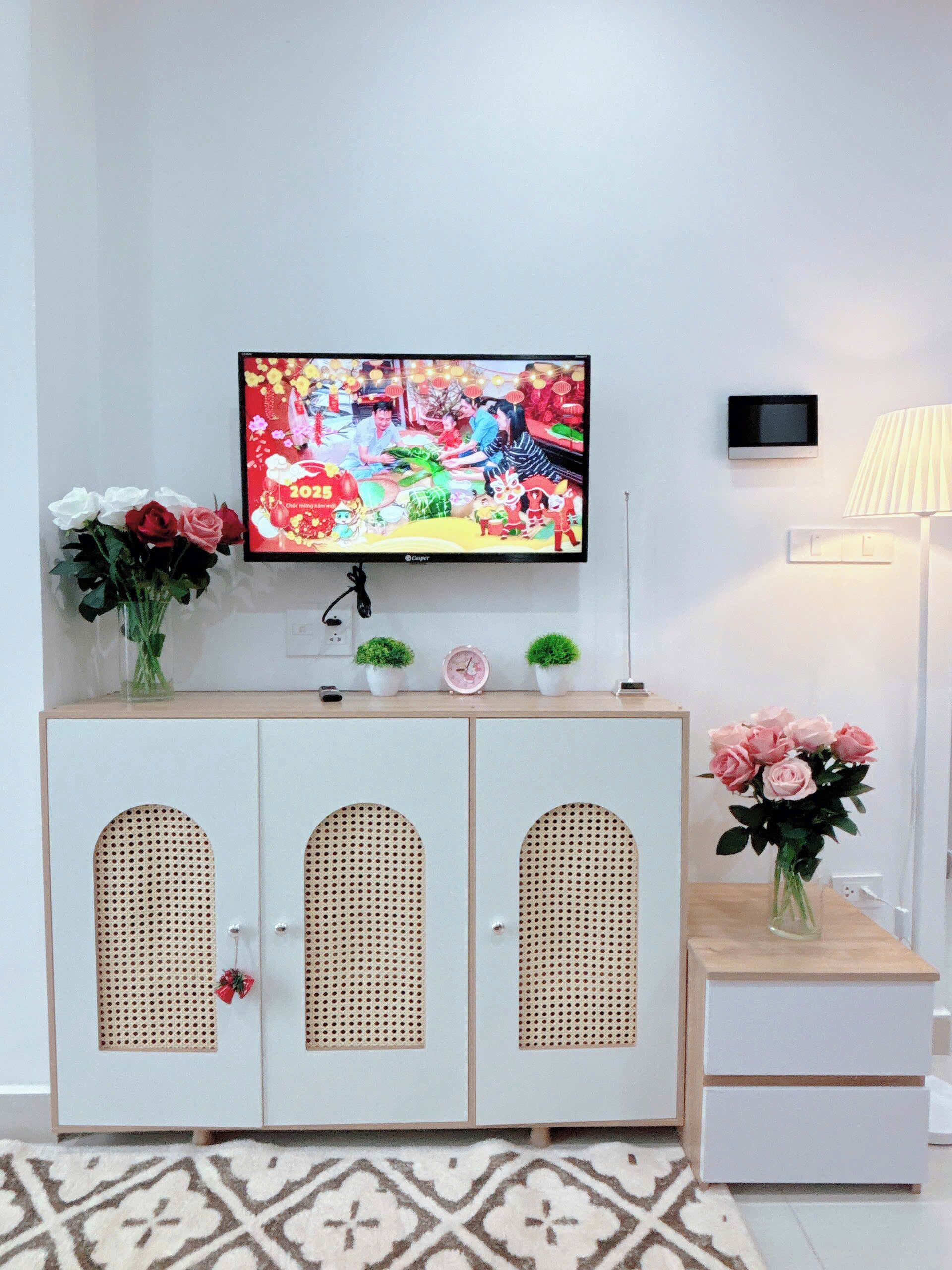 Une pièce avec un téléviseur fixé au mur, un meuble contenant des objets décoratifs, une lampe et un tapis à motifs.