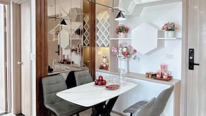 Un'area pranzo moderna con tavolo bianco, sedie imbottite grigie e una parete decorata con motivi geometrici e composizioni floreali.