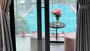 Una stanza con vista sulla piscina, un tavolo con fiori e un balcone con pouf.