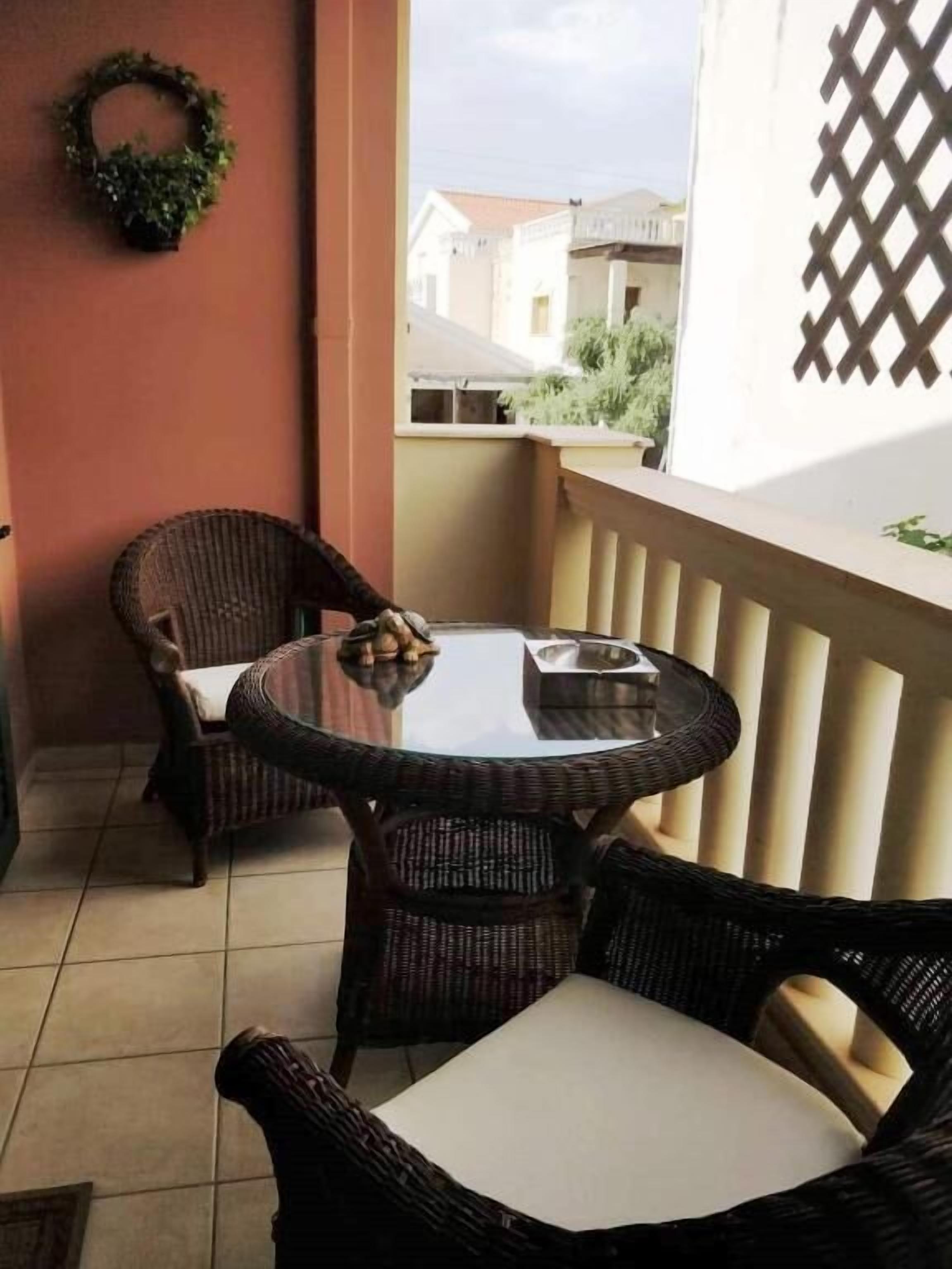 A balcony with wicker furniture, a small table, and a view of buildings in the background.