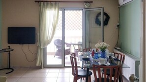 A room with a dining table, chairs, a TV, and a sliding glass door leading to an outdoor area with wicker furniture.