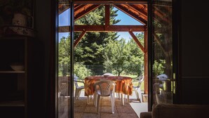 A view through a doorway to an outdoor patio area with a table and chairs, surrounded by greenery.