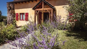 A traditional house with a wooden porch, a stone wall, and purple flowering plants in the foreground.