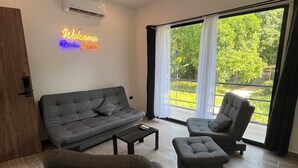 A modern living room with a grey sofa, two armchairs, and a coffee table. A neon sign reads "Welcome Tierra Boulka."