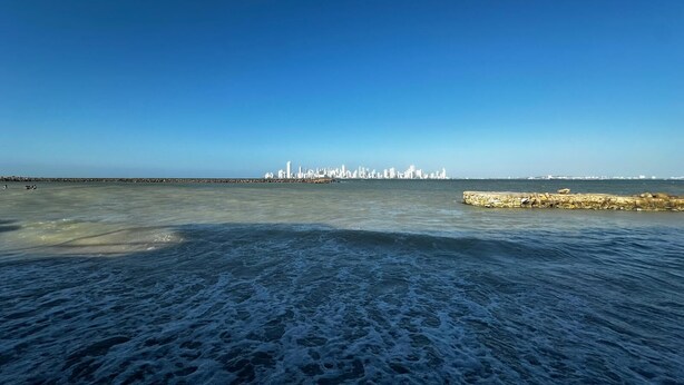 A coastal view with a stone jetty and a distant city skyline.