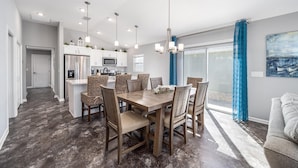 A modern kitchen with white cabinets and stainless steel appliances, a dining area with wooden tables and patterned chairs, and a large sliding glass door leading to a balcony. - Deja Blue with a Stunning View! - 3/2 in Atwood Bungalows w/WATERFRONT BIRDS & SUNSET VIEWS (Atwood Bungalows, The VIllages)