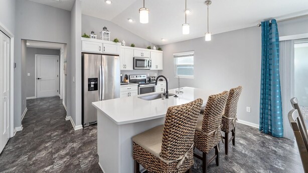 A modern kitchen with white cabinetry, stainless steel appliances, and a central island with bar stools. - Deja Blue with a Stunning View! - 3/2 in Atwood Bungalows w/WATERFRONT BIRDS & SUNSET VIEWS (Atwood Bungalows, The VIllages)