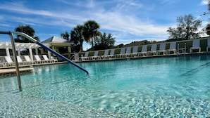 A clear swimming pool with a blue diving board, lounge chairs, and a covered seating area. - Deja Blue with a Stunning View! - 3/2 in Atwood Bungalows w/WATERFRONT BIRDS & SUNSET VIEWS (Atwood Bungalows, The VIllages)